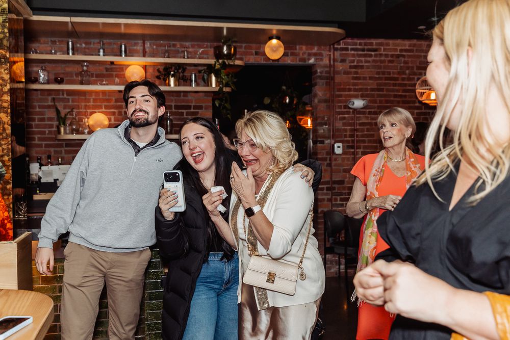 Group of friends laughing and socializing at a trendy brick-wall bar or restaurant during a casual evening gathering.