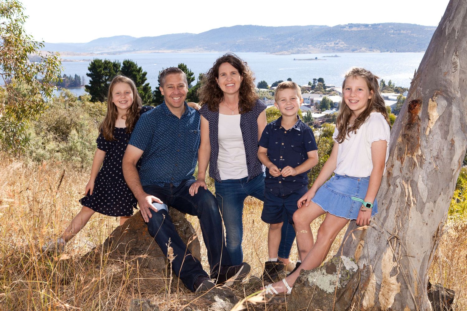 A group of people in casual attire pose together outdoors against a natural backdrop on a sunny day.