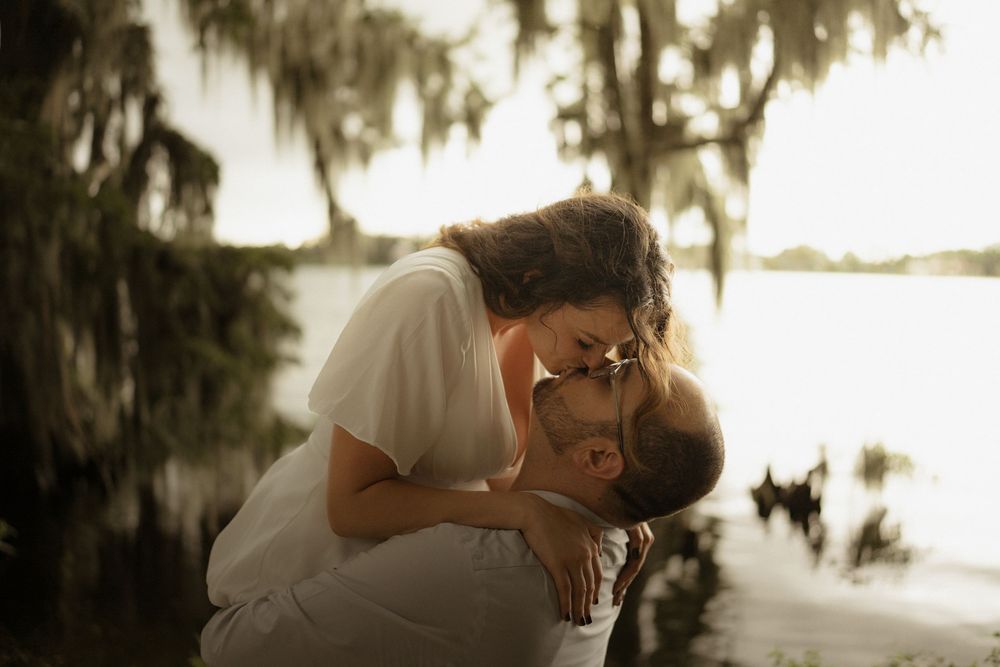 Romantic couple shares tender moments in sepia-toned wedding photos beneath Spanish moss draped trees.