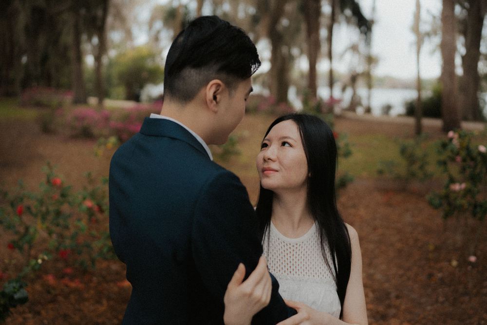 A romantic couple embraces on a path lined with autumn trees and fallen red leaves during an outdoor photo session.