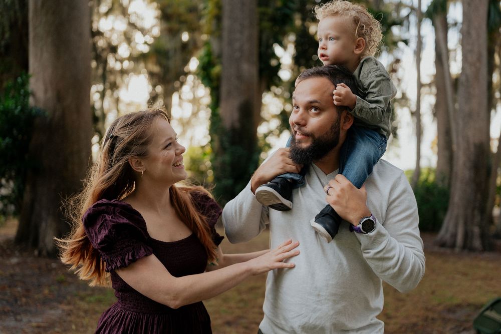 A family enjoys a playful moment together in a wooded setting during golden hour.