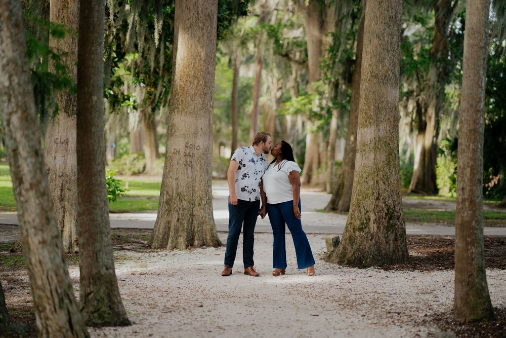 A couple walks hand in hand down a tree-lined path covered in Spanish moss at a romantic outdoor location.