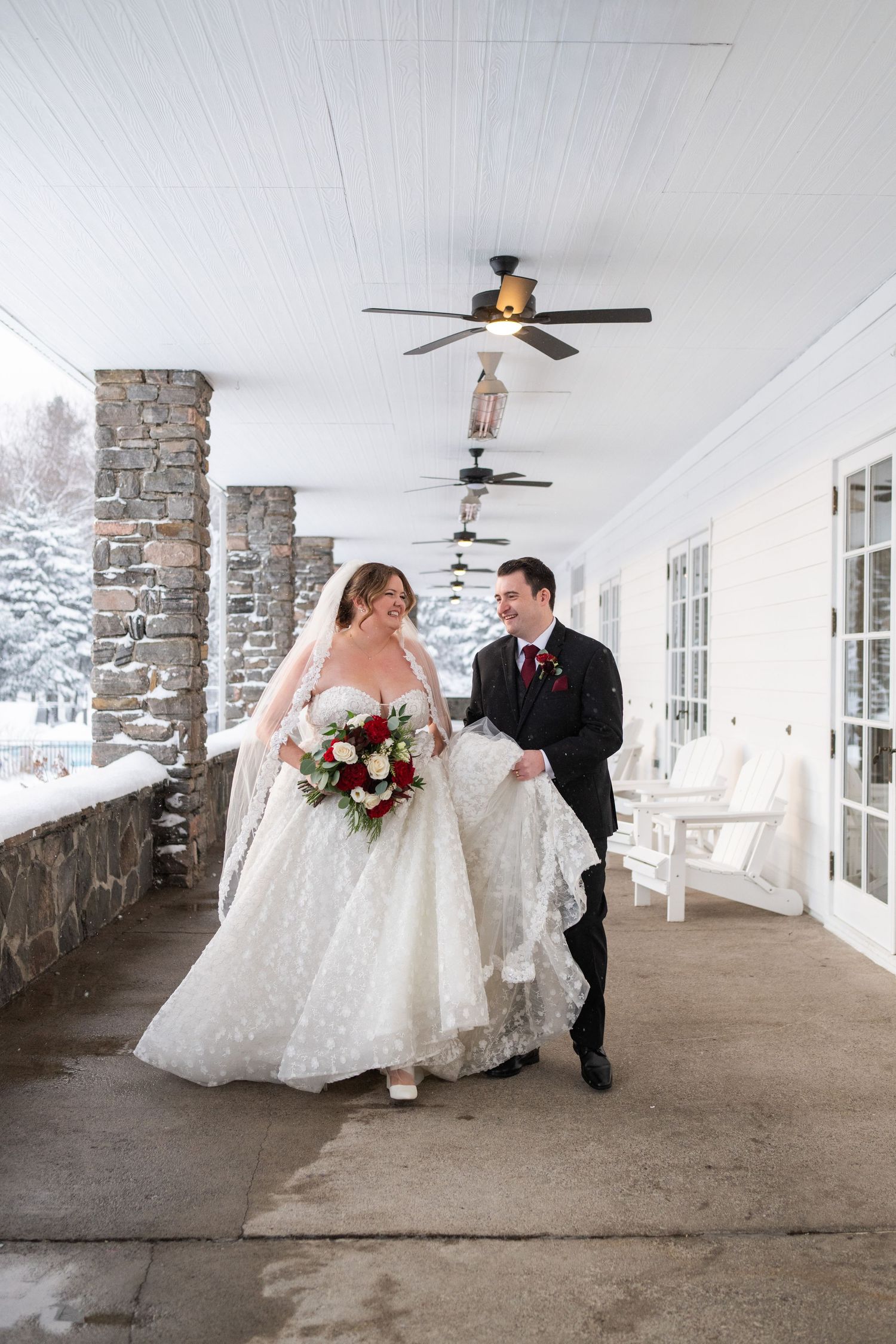 A winter wedding scene on a covered porch with stone pillars and snowy landscape in the background.