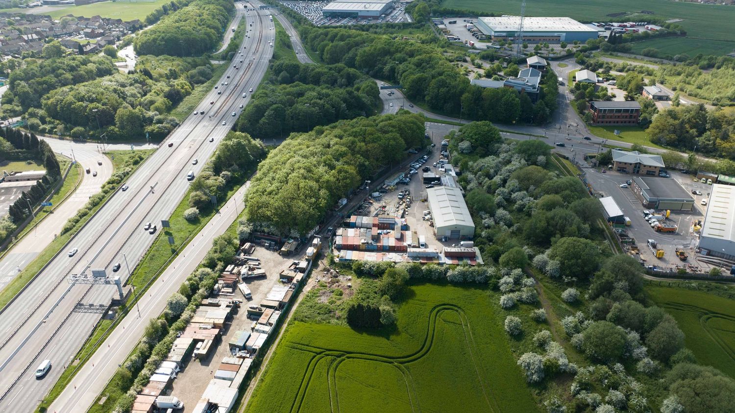 Aerial view of a green industrial area beside a major highway, surrounded by lush trees and fields.