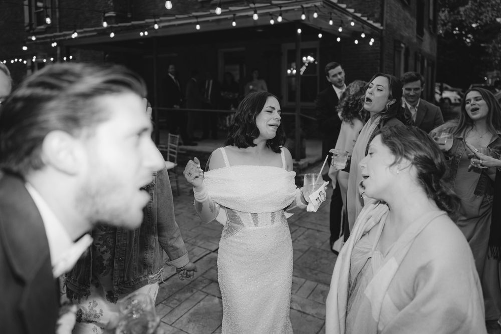 Wedding guests dance and celebrate under string lights at an evening reception.