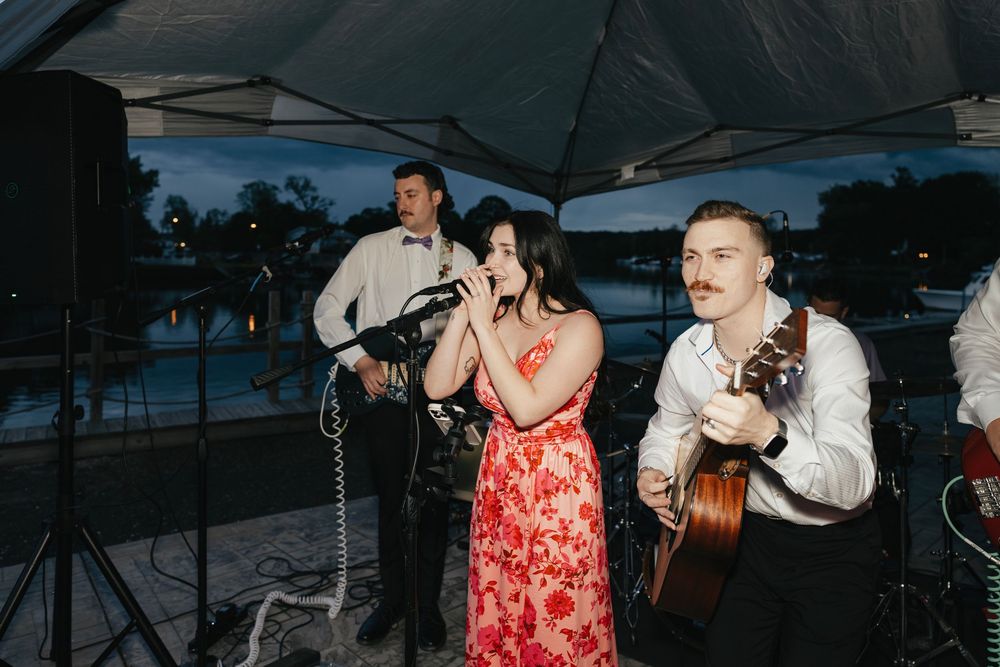 Live band performing at an outdoor wedding reception with instruments and microphones.