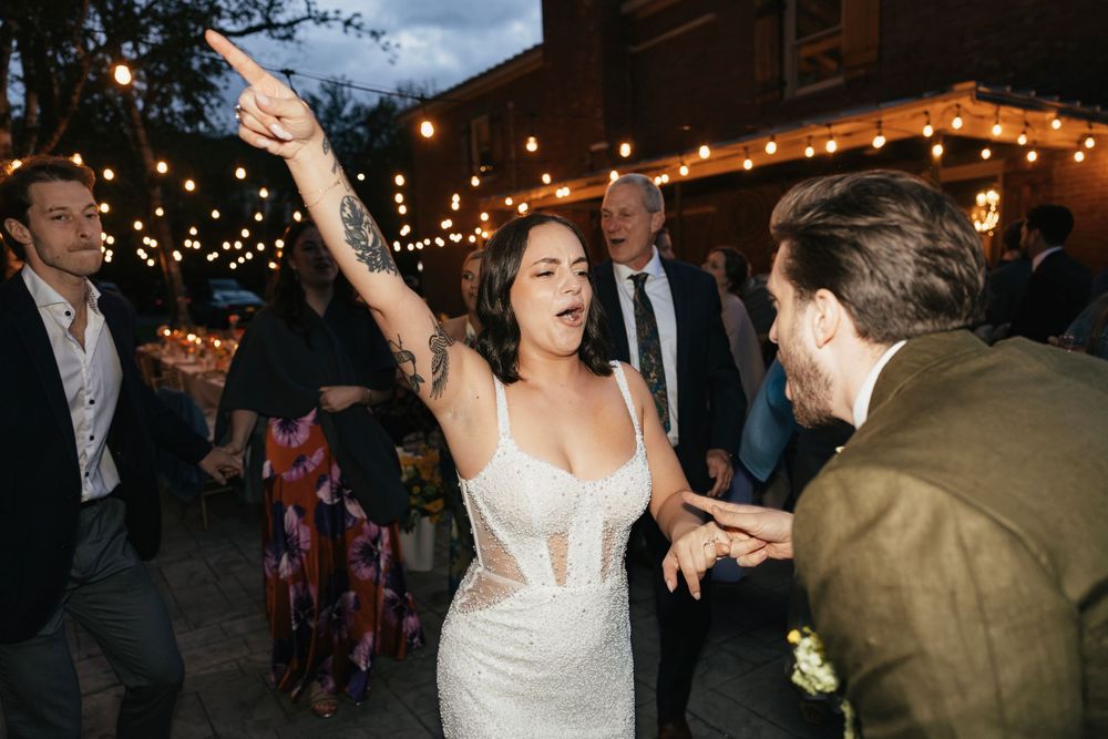 Wedding celebration with guests dancing under string lights at an outdoor evening reception.