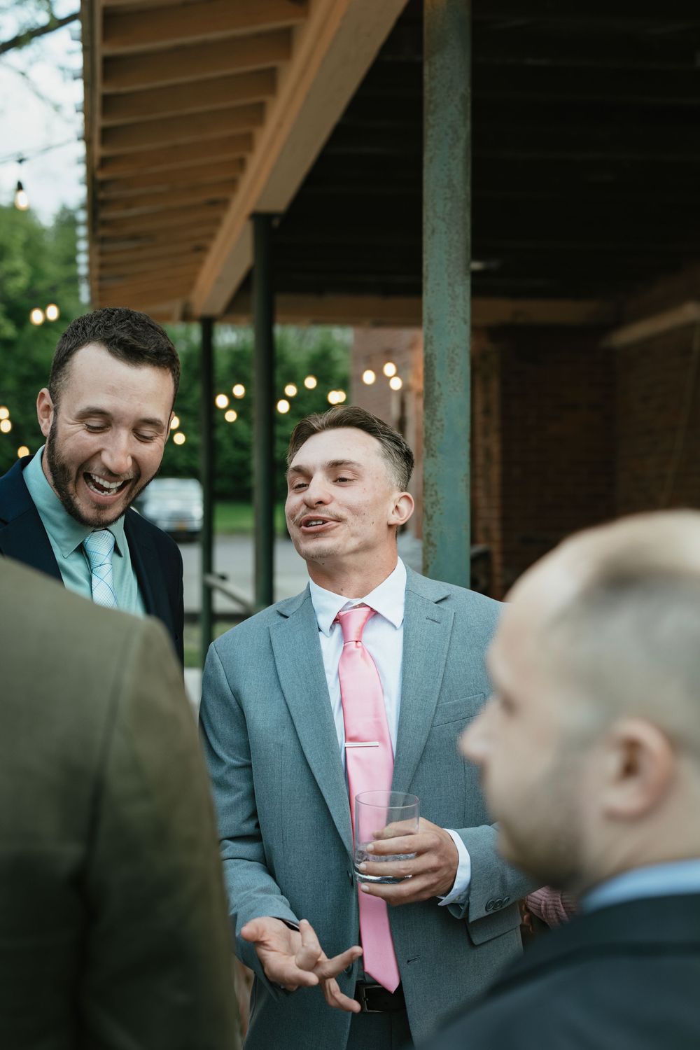 Wedding guests enjoying drinks and conversation under a covered outdoor patio with string lights.