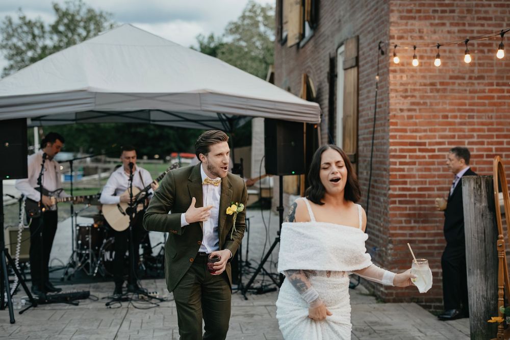 Outdoor wedding celebration under white tents with brick building backdrop and string lights.