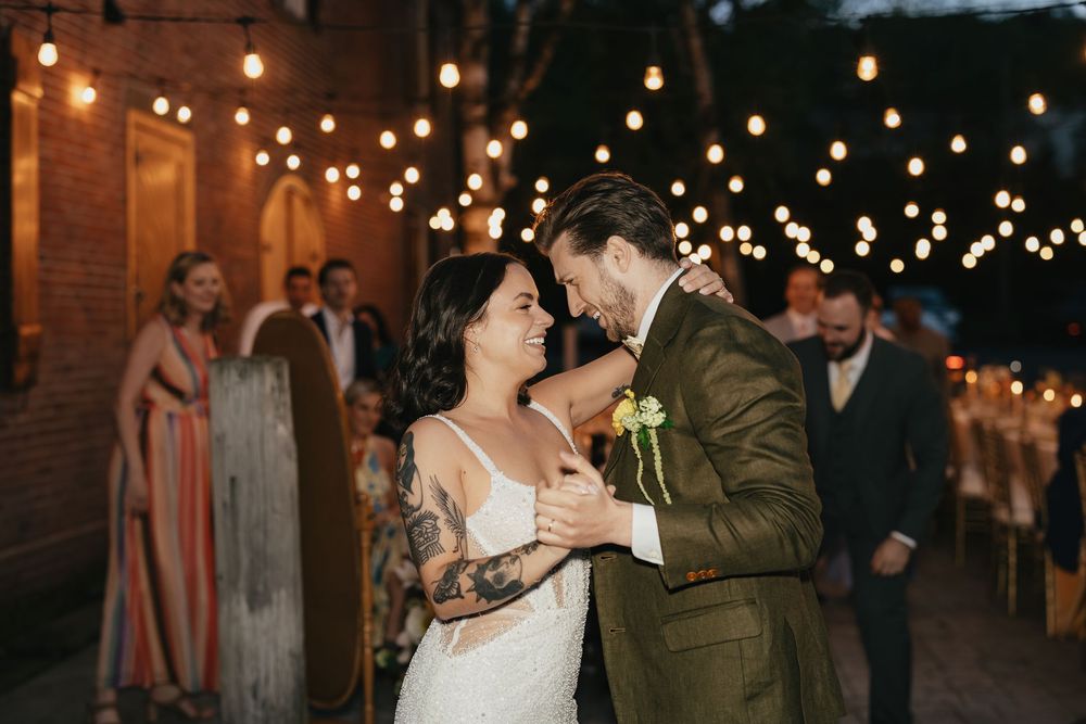 A romantic evening wedding reception with string lights creating a warm ambiance as people dance.