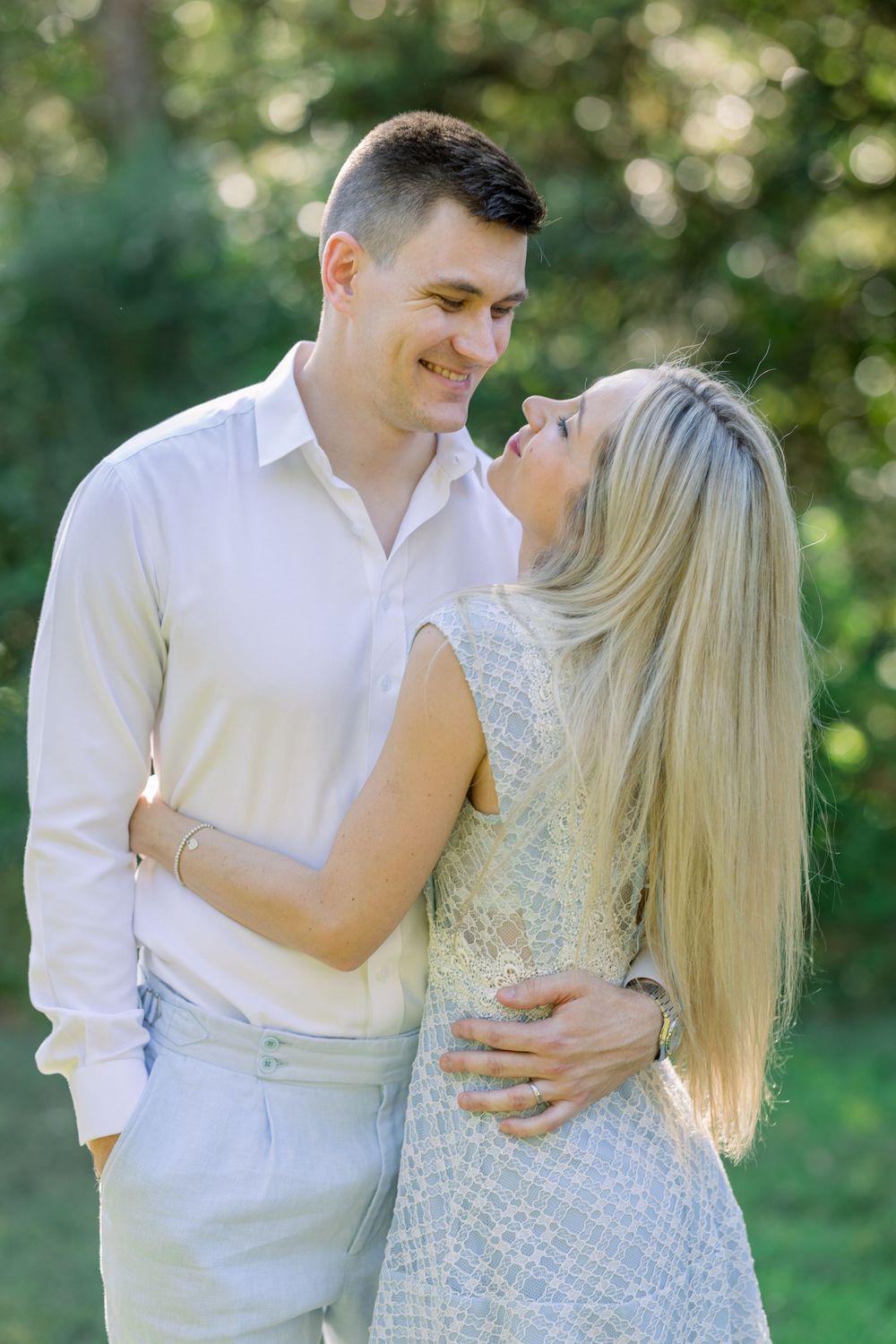 Couple in white outfits share tender moments in a sunlit garden setting.