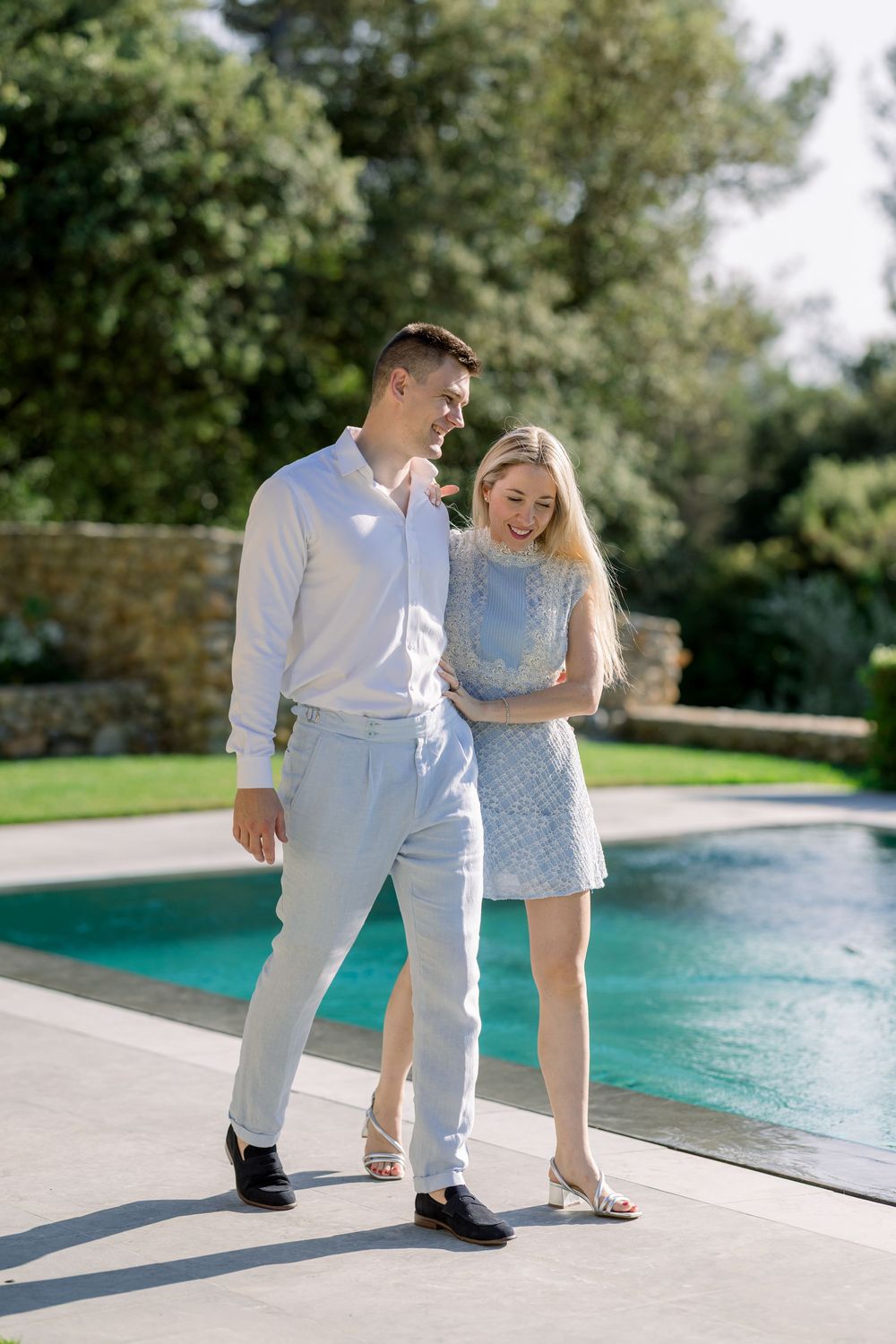 Couple shares playful moments by modern swimming pool in bright daylight.