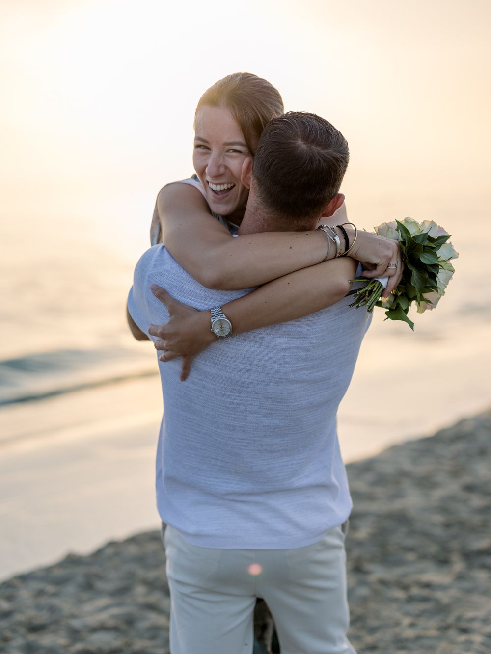 A joyful embrace captured on the beach at sunset with warm golden lighting.