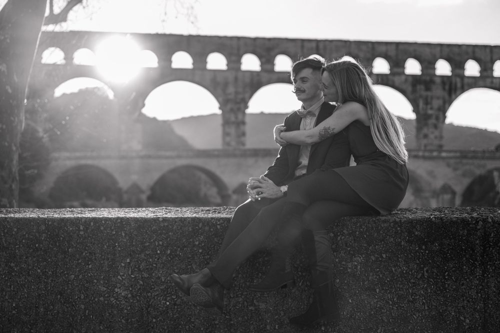 Silhouetted couple embraces near stone archway during golden hour.