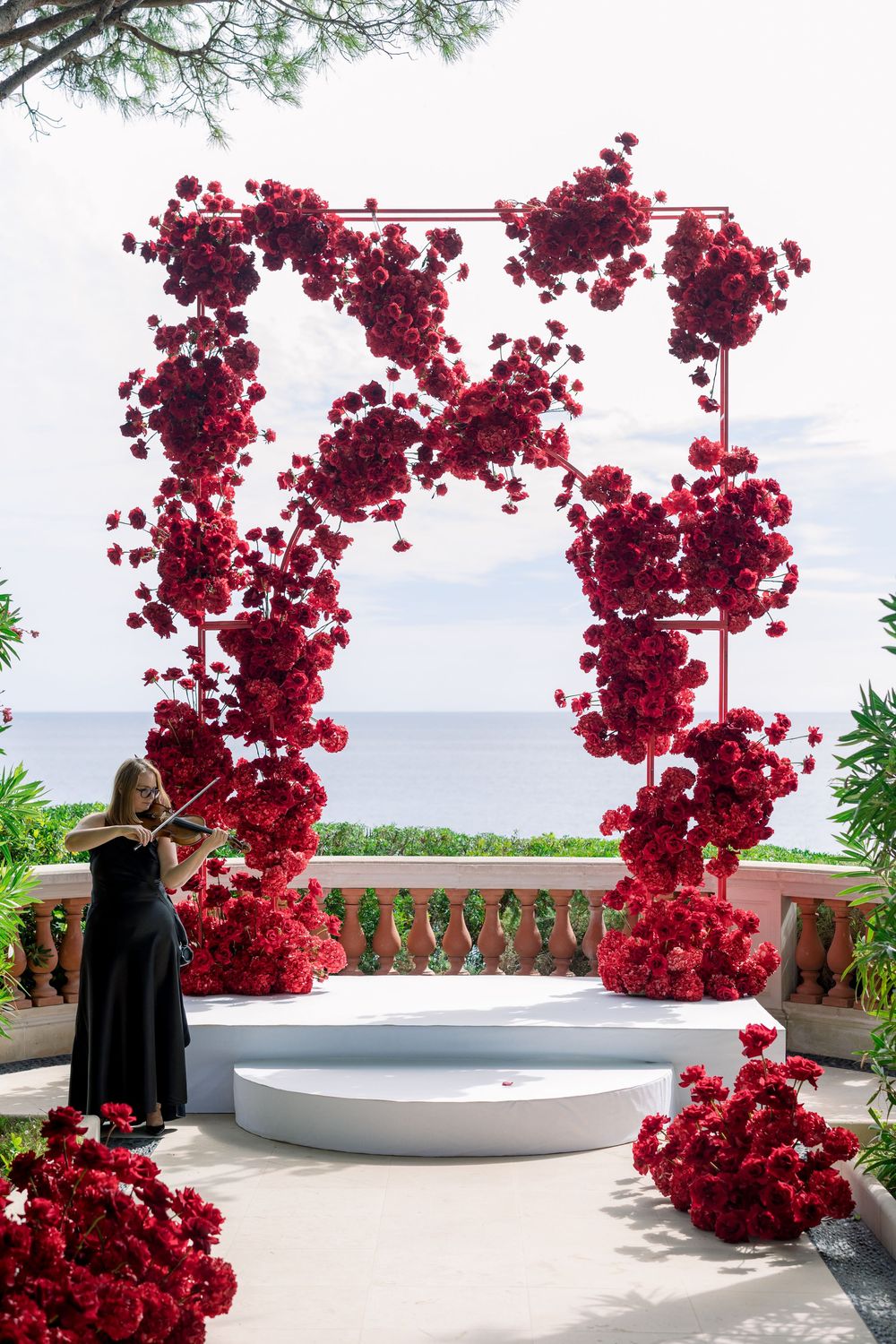 Beautiful red floral arch installation against white balcony with ocean view.