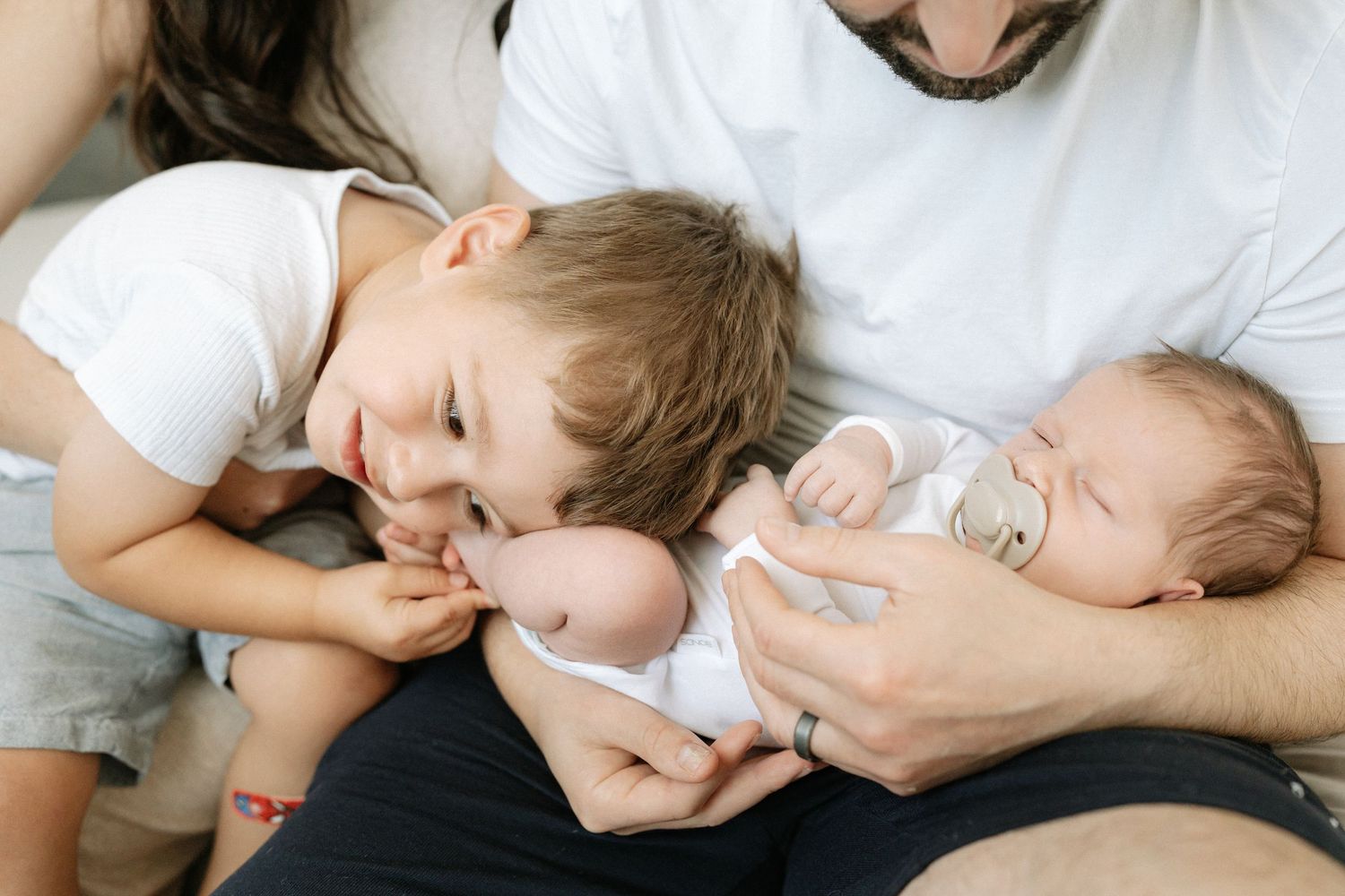 Newborn being held in father's arms with toddler interacting with the baby.