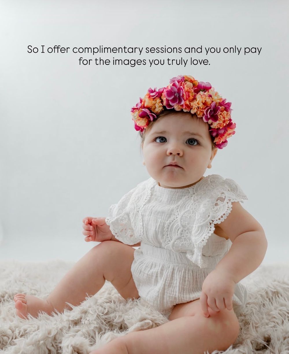 Baby wearing white lace dress and pink floral crown sits on fluffy rug during professional photo session.