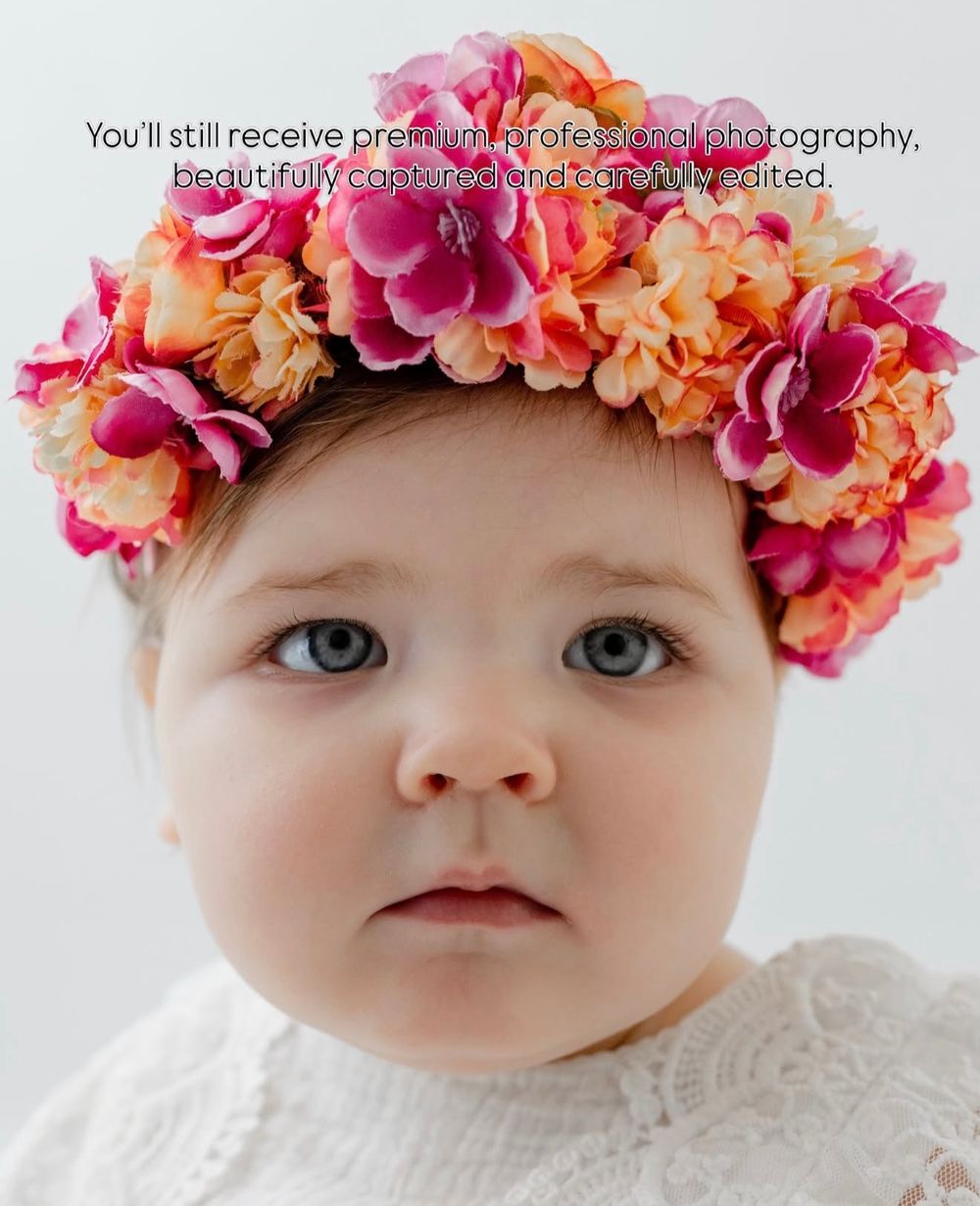 Close up portrait of baby adorned with vibrant pink and peach floral crown against white background.