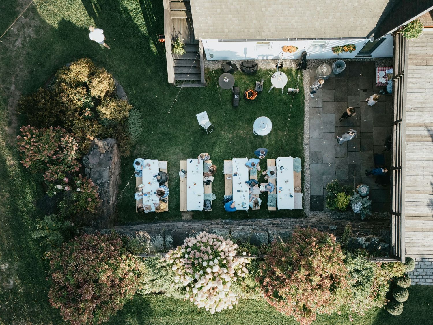 Aerial view of a backyard swimming pool with surrounding patio furniture and lush landscaping during summer.