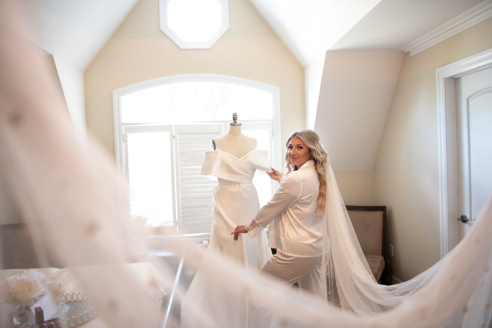 Bride adjusting her wedding gown on a mannequin in a bright dressing room before the ceremony.