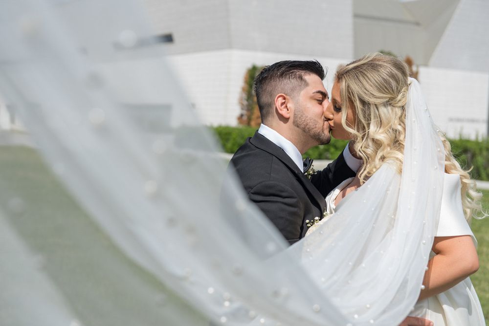Bride and groom sharing a romantic kiss framed beautifully by the brides flowing white wedding veil.