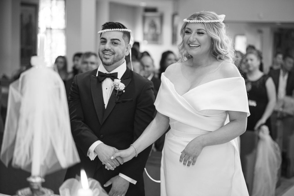 Bride and groom smiling joyfully while holding hands during their wedding ceremony inside a decorated church.