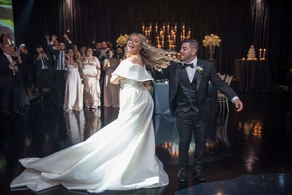 Bride and groom sharing joyful first dance in stunning white gown with flowing train at wedding reception.