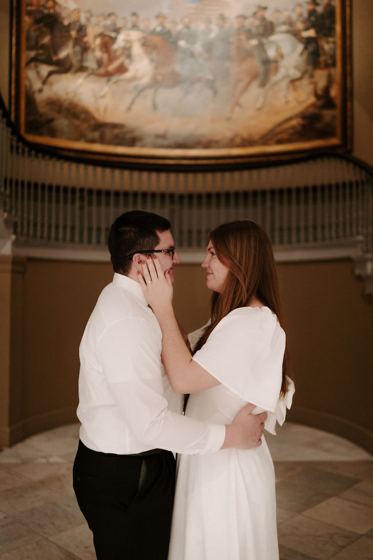 Couple gazes lovingly at each other beneath a large equestrian battle painting in a museum rotunda.