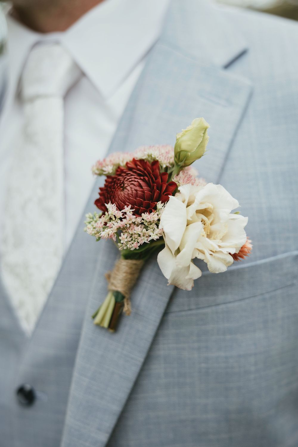 Close-up view of delicate white and burgundy floral boutonnieres pinned to gray suit jackets.