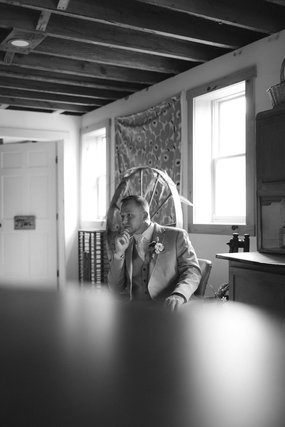A black and white interior scene showing a contemplative figure seated by a window.