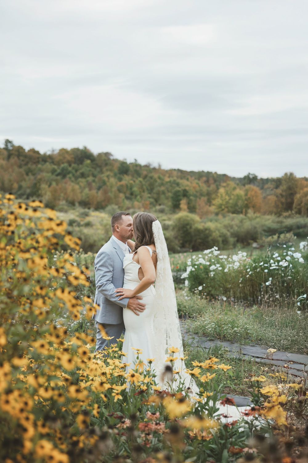 A couple shares an intimate moment among wildflowers and autumn foliage in a scenic outdoor setting.