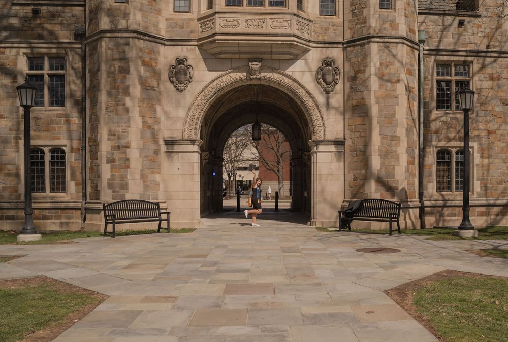 Historic stone university building archway with benches and flagstone courtyard on a quiet campus day.