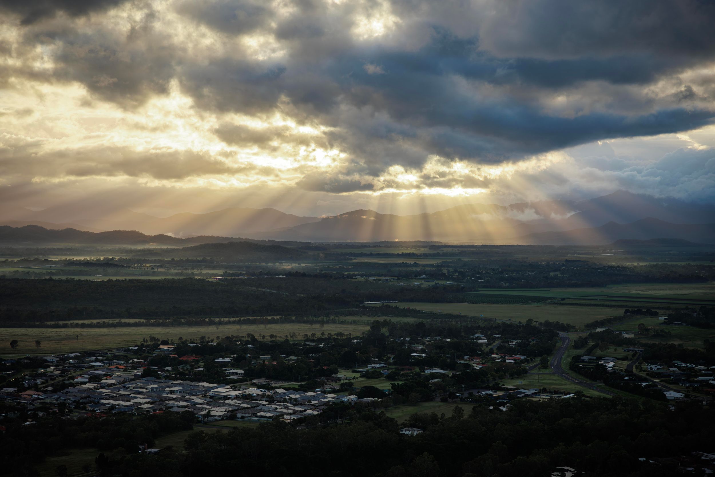 Dramatic sunrays breaking through storm clouds over a valley town with mountains in the background at sunset. Cairns Australia