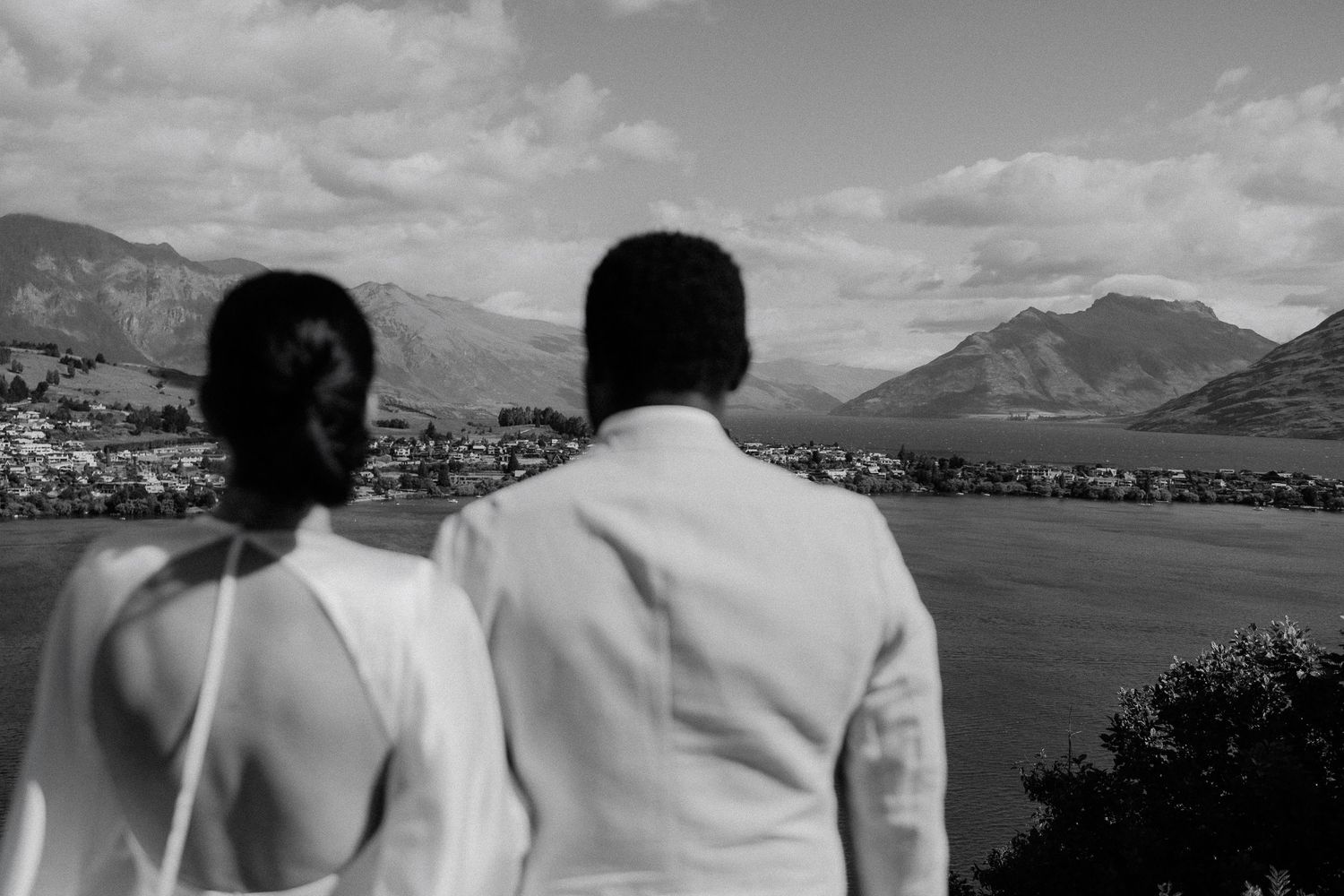 A bride and groom gaze at a scenic mountain landscape overlooking Lake Wakatipu, Queenstown in black and white photography.