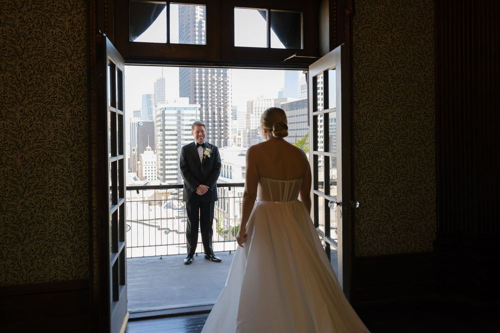 Silhouetted figures stand in front of large windows with a city skyline view.