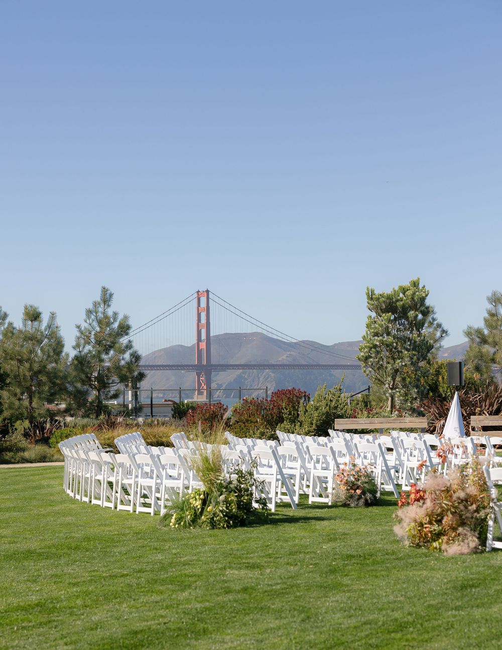 Outdoor wedding ceremony setup with white chairs and Golden Gate Bridge vista.