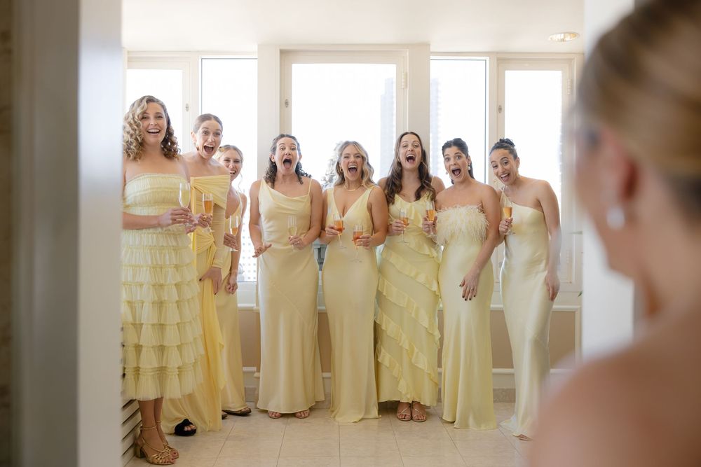 Bridesmaids in yellow dresses stand together in a row while getting ready for a wedding celebration.