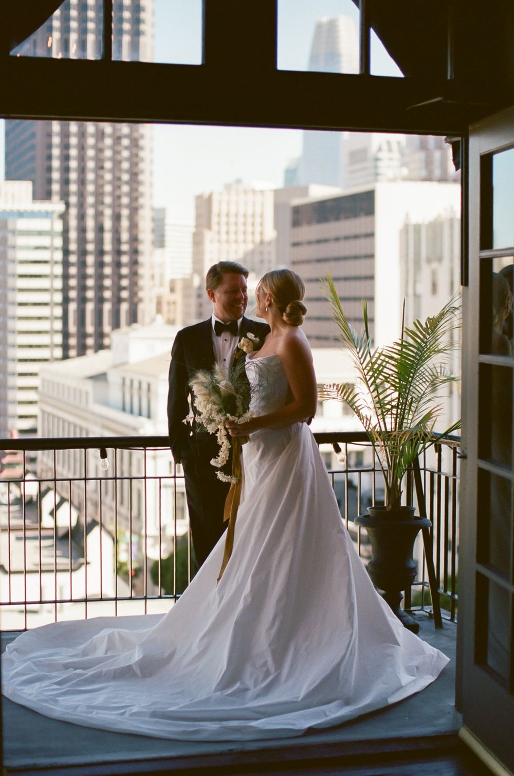 Elegant wedding couple shares an intimate moment on a city balcony with skyline views.