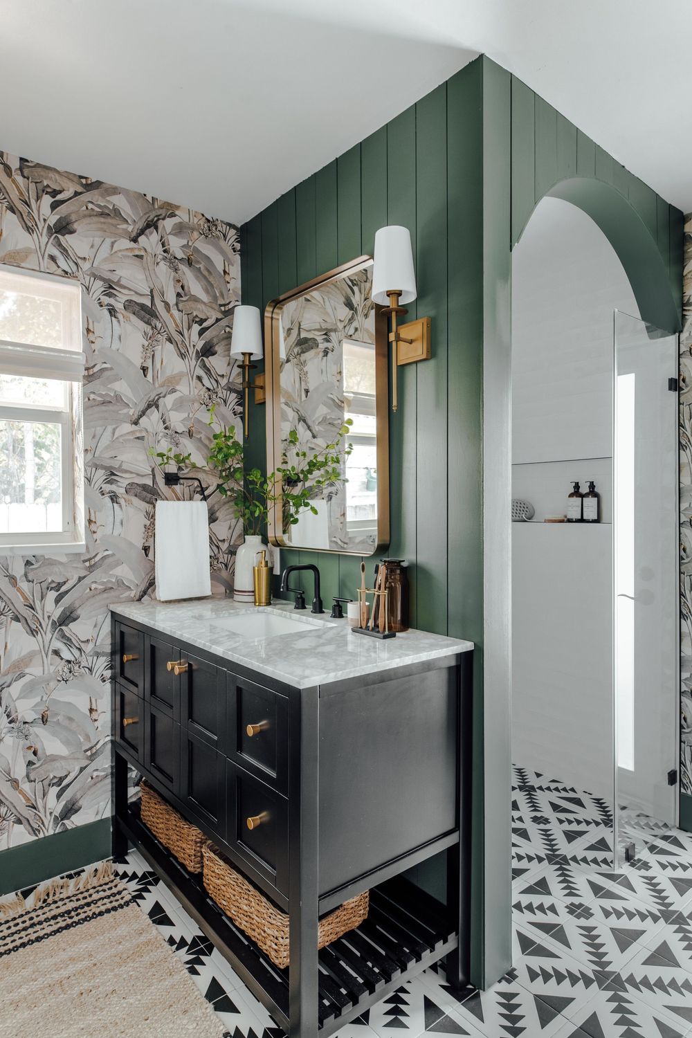 Dark vanity with marble top, green shiplap wall, bold patterned floor tiles, and tropical wallpaper.