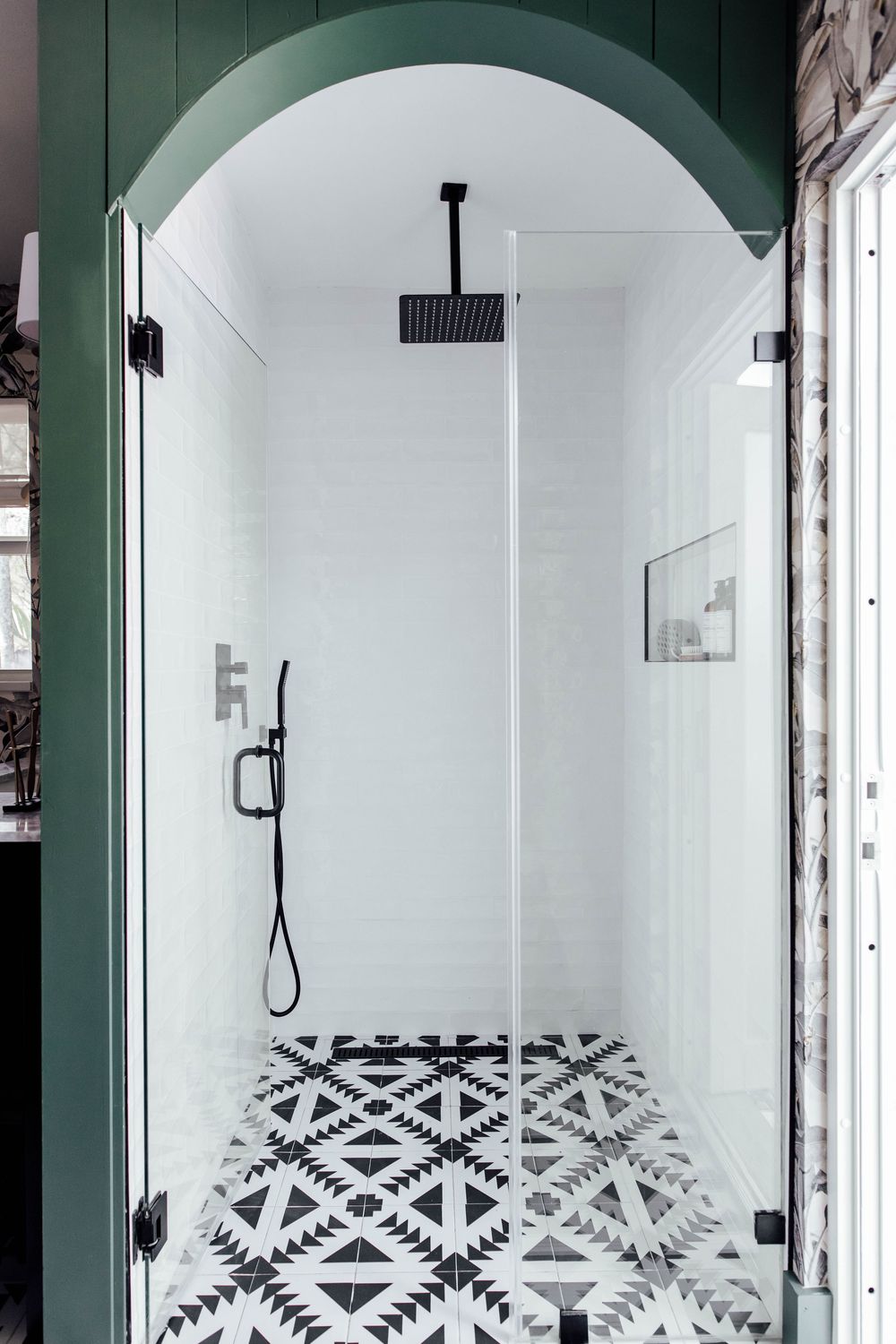 Arched glass shower enclosure with black fixtures, geometric patterned floor tiles, and green trim.