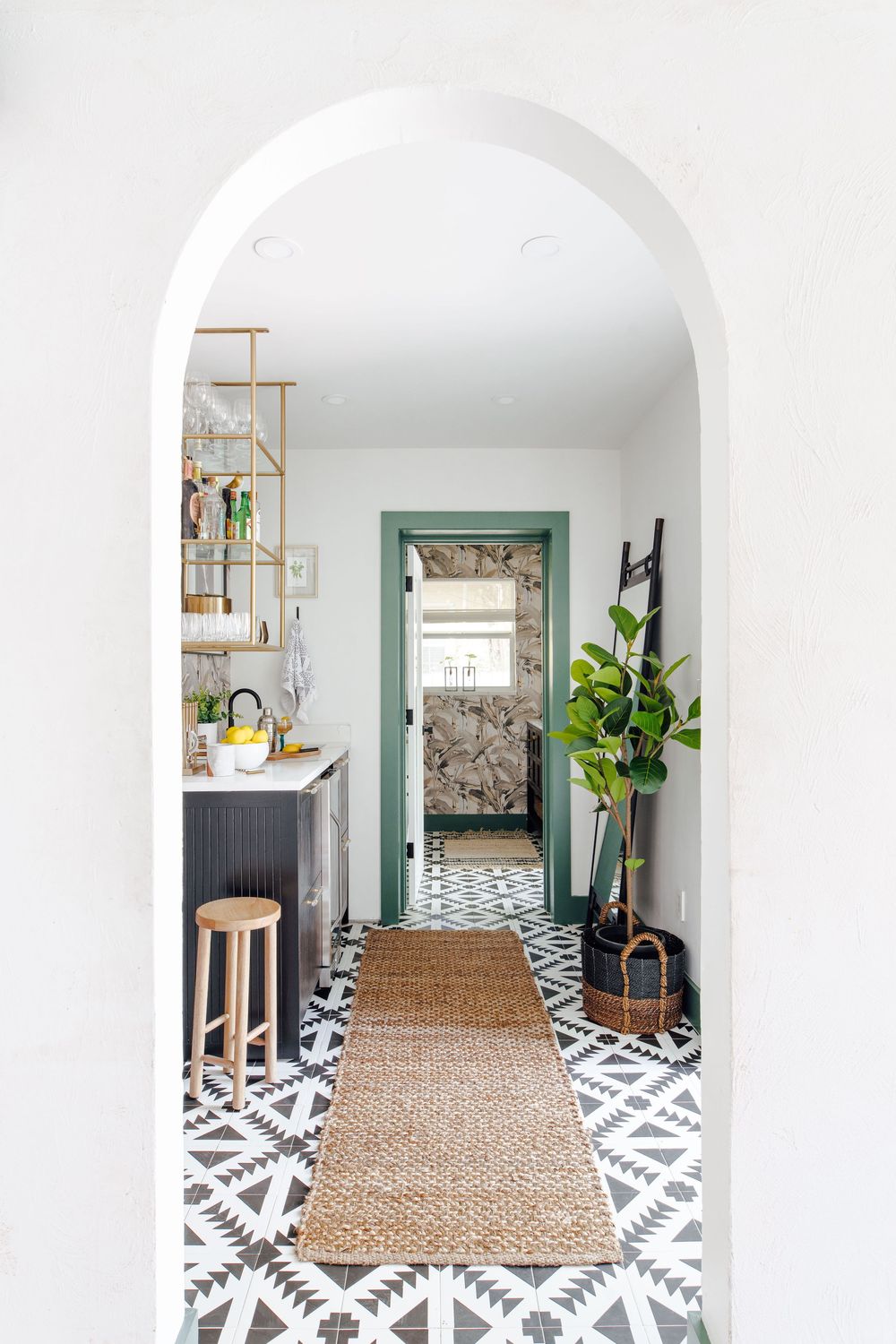 Bright hallway with black and white geometric floor tiles, jute runner, arched entry, and green door.