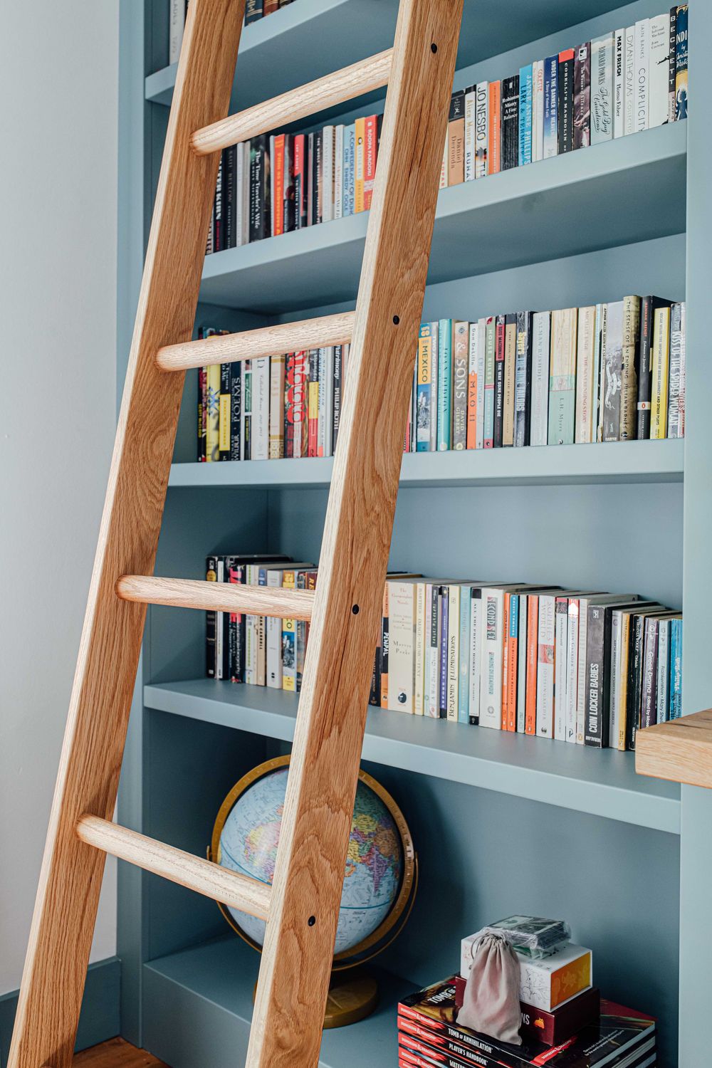 Wooden library ladder leaning against blue built-in bookshelf filled with colorful books and globe.