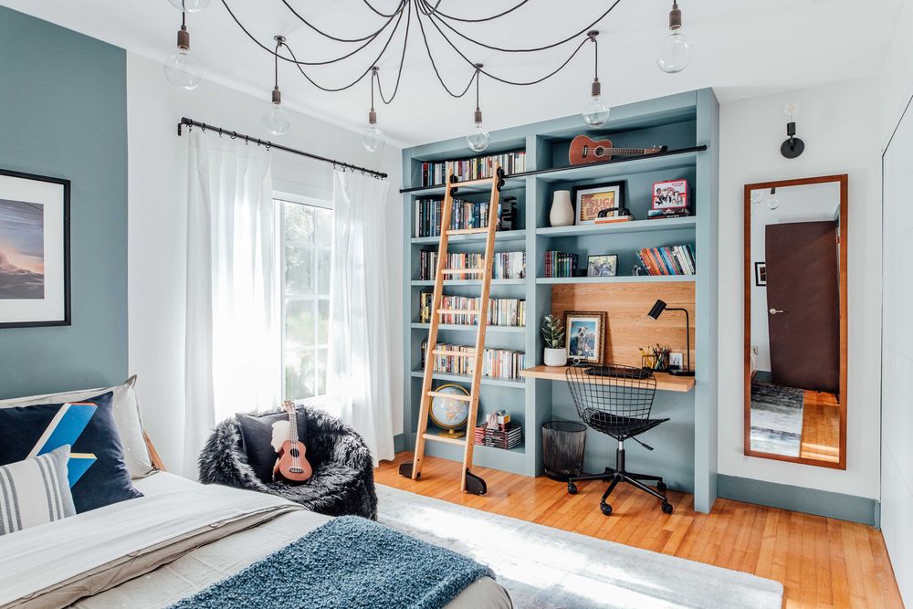 Blue bedroom featuring built-in bookshelves with wooden ladder, wire desk chair, bean bag, and pendant light fixture.