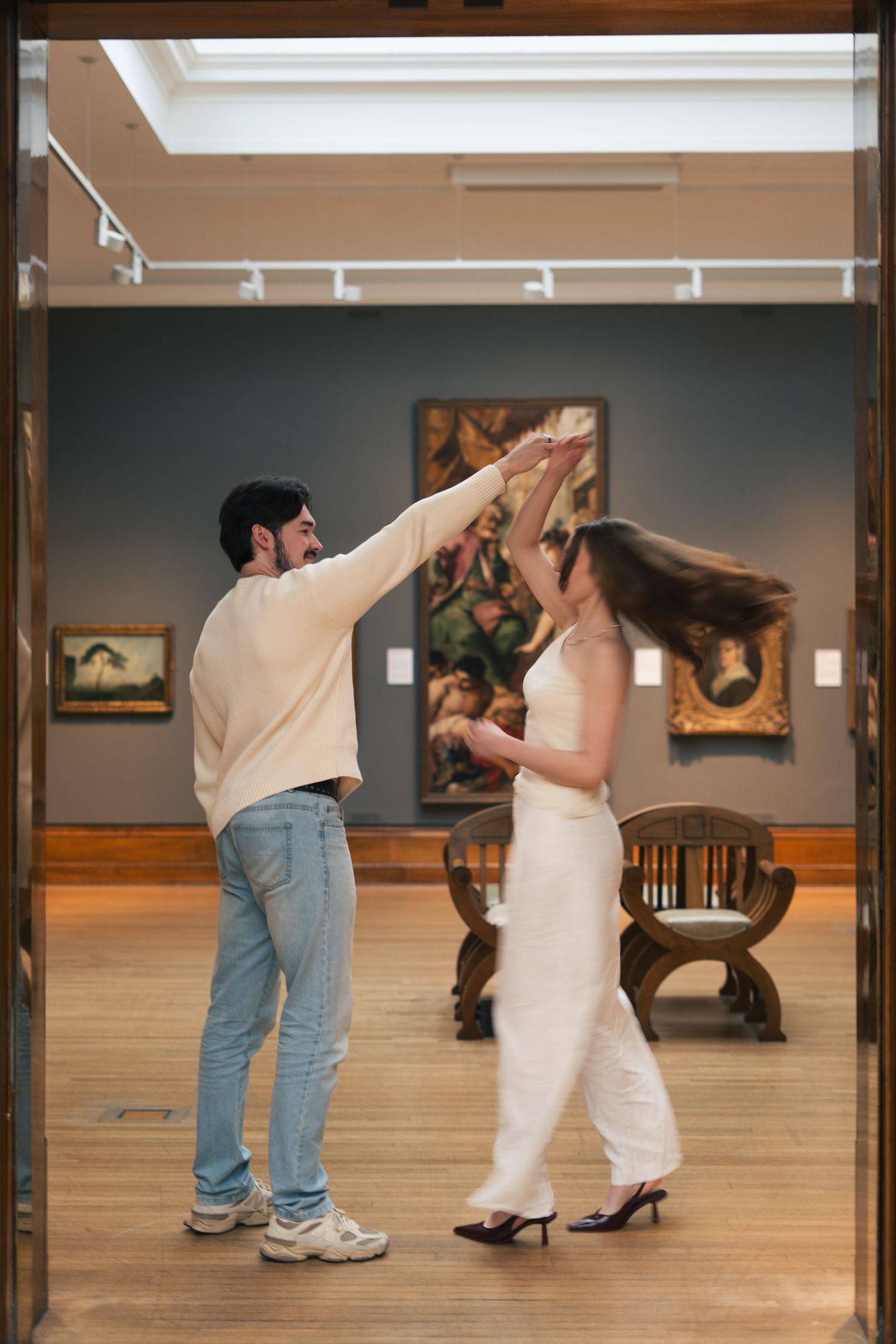 Couple dancing together in Ferens Art gallery with classic paintings on gray walls.