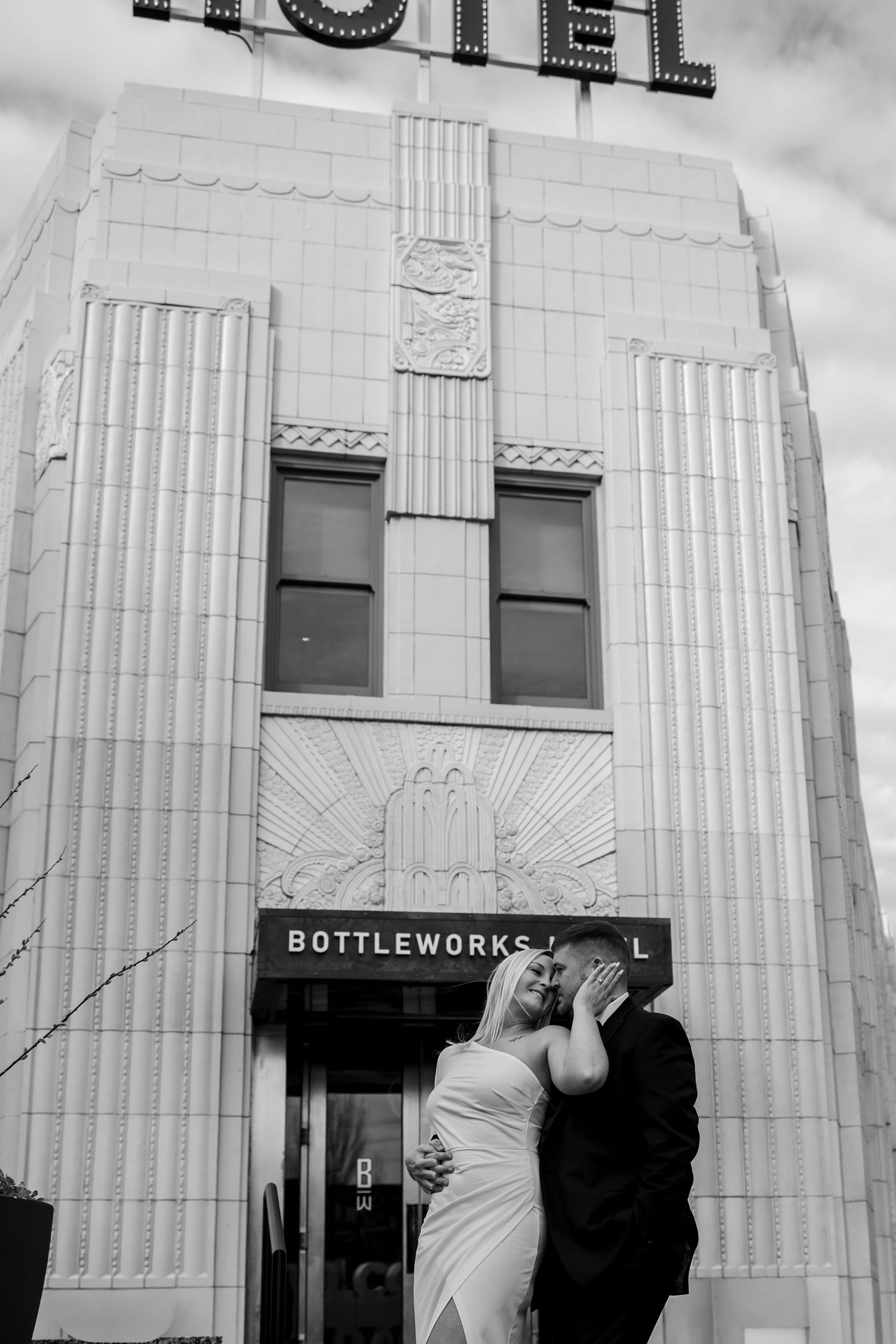 Couple in front of Bottleworks Hotel, woman touching his face, looking up at him, man looking down, Indianapolis engagement session