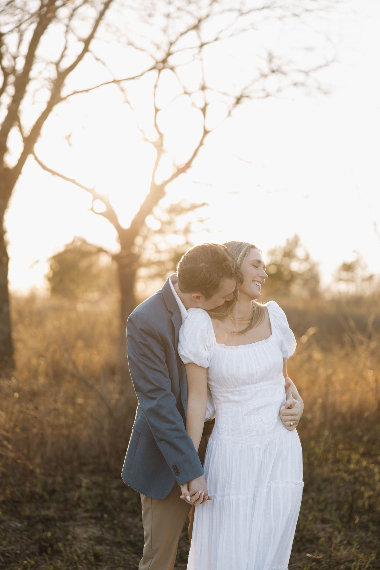 Romantic couple in wedding attire embracing during golden hour sunset in a natural outdoor setting.