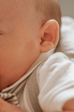 Close-up of a sleeping newborn baby's ear and cheek, wearing a striped outfit in soft natural light.