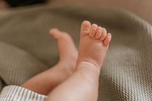 Close-up of tiny newborn baby feet resting on a soft green knit blanket.