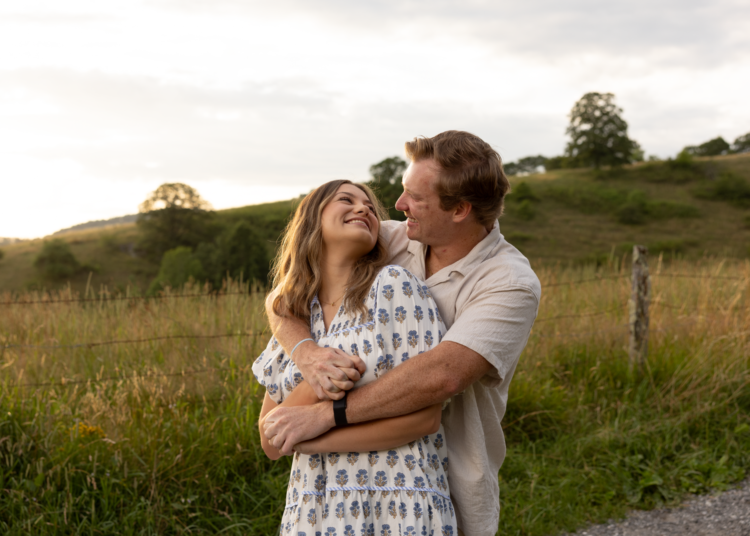 Happy couple embracing in a lush green field at golden hour, smiling and holding each other close.