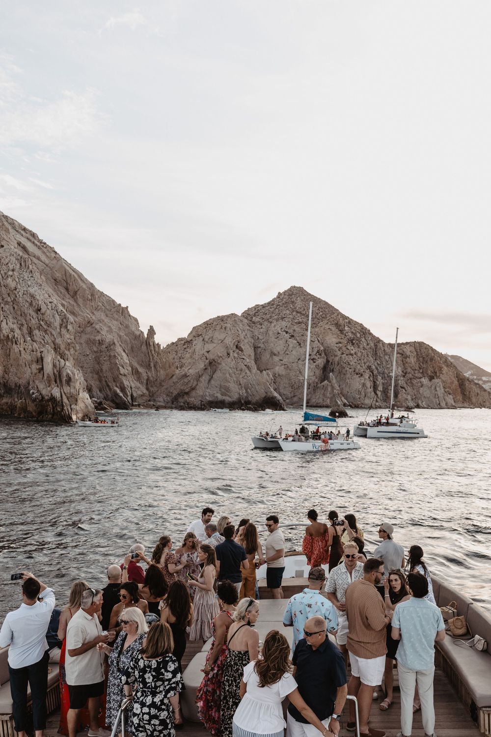 Scenic boat tour with guests gathered on deck viewing rugged coastal cliffs and rock formations at sunset.